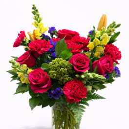 Mixed bouquet of red roses, carnations, and yellow snapdragons in a glass vase