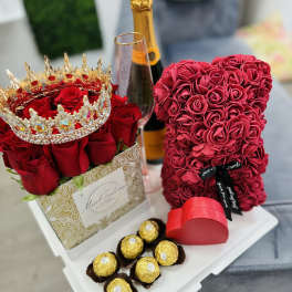 Red rose arrangement with a jeweled crown, champagne bottle, heart box, and chocolates