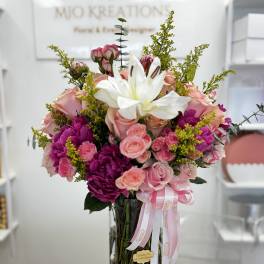 Pink and white flower bouquet in a tall glass vase with ribbon