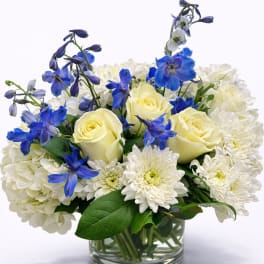 White and pale yellow roses with blue flowers in a glass vase