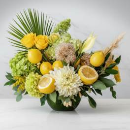 Yellow roses and white blooms arranged with lemons in a vase