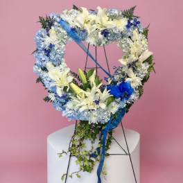 Heart-shaped floral wreath with white lilies and blue flowers on a stand