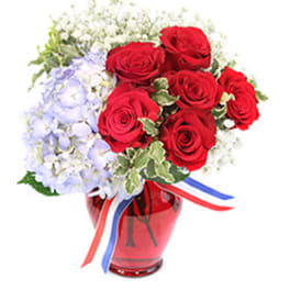Red roses and pale blue flowers in a red glass vase with ribbon