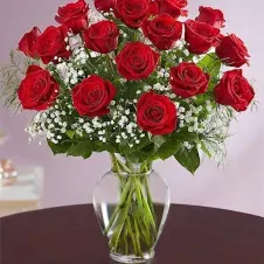 Red roses arranged in a clear glass vase with white filler flowers