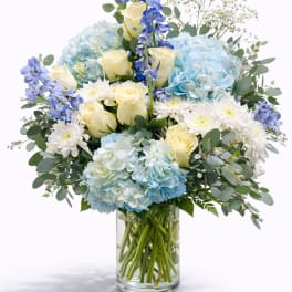 Blue hydrangeas, ivory roses and white mums in a clear glass cylinder vase