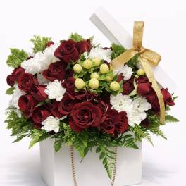 Red roses and white daisies in a white gift box with a gold ribbon