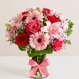 Pink and red mixed flower bouquet in a glass vase with a pink ribbon