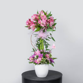 Tall pink flower arrangement in a white vase with a ribbon bow