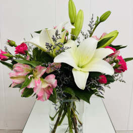 White lilies and pink flowers arranged in a clear glass vase