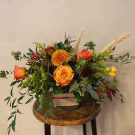 Orange and red roses in a square container with greenery