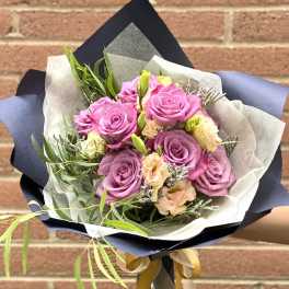 Bouquet of pink and lavender roses with peach accents in paper wrap