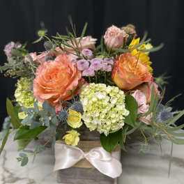 Mixed bouquet of peach roses, hydrangea, and yellow blooms in a wooden box
