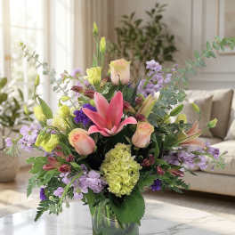 Mixed bouquet of pink lilies, roses, and lavender flowers in a glass vase