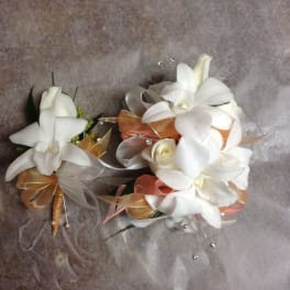 Two white floral corsages with ribbon accents on a textured background
