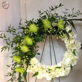 Circular floral wreath on a black stand with white and green blooms
