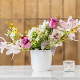 Pink and white orchid bouquet in a white vase with a small candle