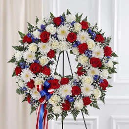 Heart-shaped floral wreath with red, white, and blue flowers on a stand