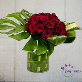 Red roses arranged in a glass vase with large tropical leaves