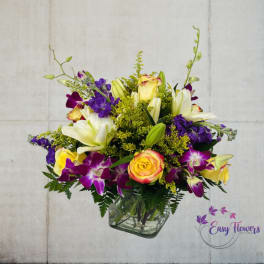 Mixed bouquet of lilies, roses, and purple orchids in a glass vase