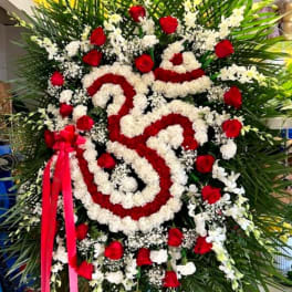 Large standing floral wreath with red and white flowers and a pink ribbon