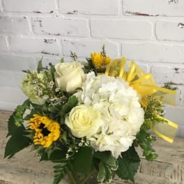 Bouquet of white roses, hydrangea, and sunflowers in a glass vase with yellow ribbon