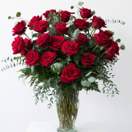 Red roses arranged in a clear glass vase with airy greenery