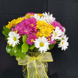 Bouquet of white, yellow, and pink daisies in a glass vase with a yellow ribbon