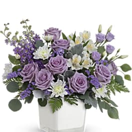Lavender roses and white flowers in a clear square vase