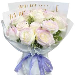 Bouquet of pale pink and white roses wrapped in white paper with a purple ribbon