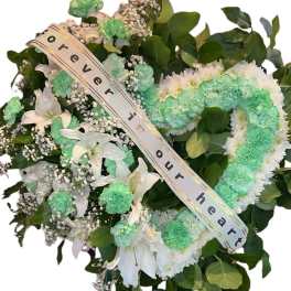 Heart-shaped floral wreath on an easel with a memorial ribbon