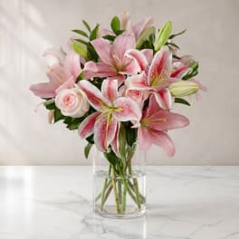 Pink lilies and roses arranged in a clear glass vase