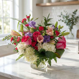 Mixed bouquet of pink roses, lilies, and hydrangeas in a clear glass vase