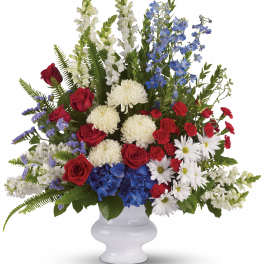 Red roses, white mums, blue flowers, and white snapdragons in a white vase