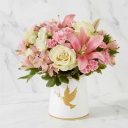 Pink and white flowers arranged in a white vase with a gold dove design.