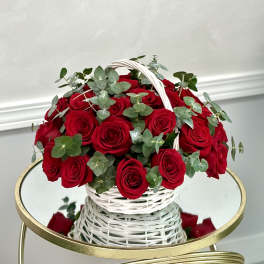 Round basket of red roses with eucalyptus in a white woven handle basket on a mirrored table