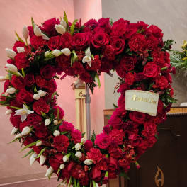 Heart-shaped red floral wreath with white tulips and a memorial ribbon