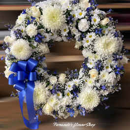 White and blue floral wreath with roses, daisies, and chrysanthemums, finished with a large royal blue bow.