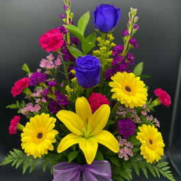 Tall mixed bouquet with yellow daisies and lily, blue roses, pink carnations in glass vase with purple bow