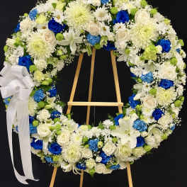 Large standing wreath of white and blue flowers with a white ribbon bow on a wooden easel