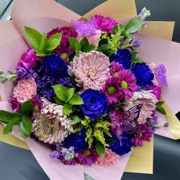Hand-tied bouquet of pink mums and blue roses wrapped in pink and yellow paper with butterfly picks