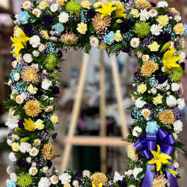 Rectangular standing wreath of yellow lilies, cream mums, and mixed small blooms with a purple bow