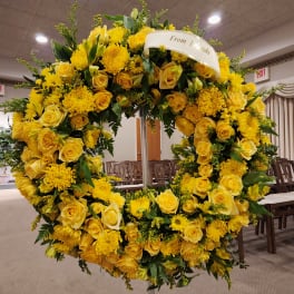 Large yellow floral wreath on a stand with a ribbon reading "From Friends"