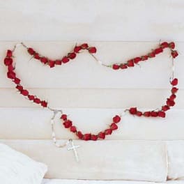 Red rose garlands draped across a white upholstered headboard with a small cross pendant