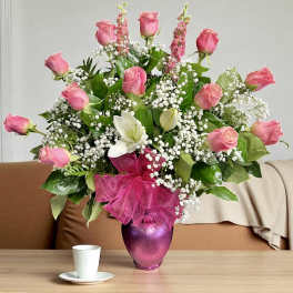 Tall arrangement of pink roses, white lilies, and baby’s-breath in a pink vase with a ribbon bow.