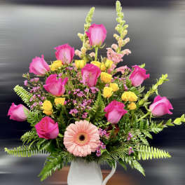 Pink roses and a peach gerbera daisy in a white pitcher vase