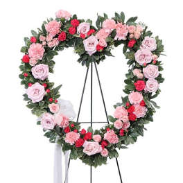 Heart-shaped floral wreath with pink and red roses on a stand