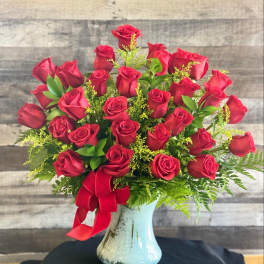Red roses arranged in a blue glass vase with a red ribbon