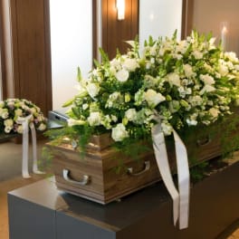 White floral casket spray with ribbons on a wooden coffin