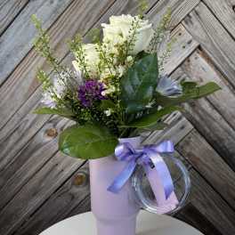 White and purple bouquet in a lavender tumbler with a ribbon