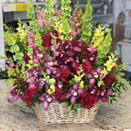 Basket arrangement of red roses, purple orchids, and green snapdragons